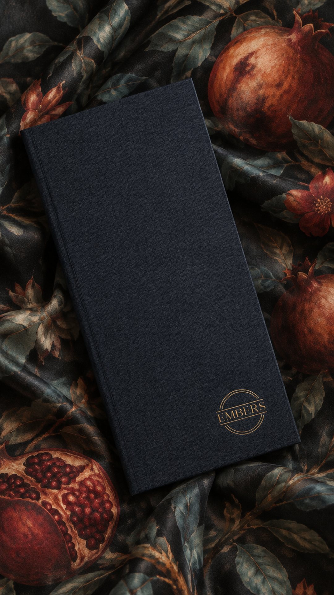 Le menu de l’Embers, son emblème de laiton sur une couverture de lin sombre, posé sur une soie aux grenades
