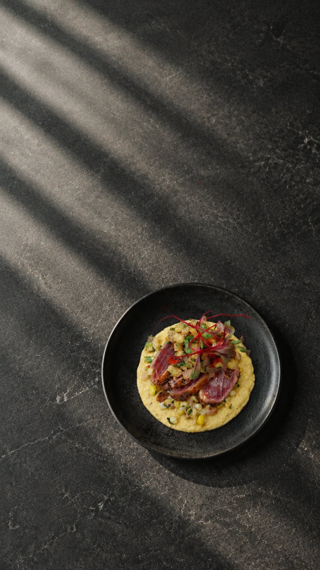 Thon saisi, salsa d’ananas et purée de maïs dans une assiette noire, sur une pierre sombre